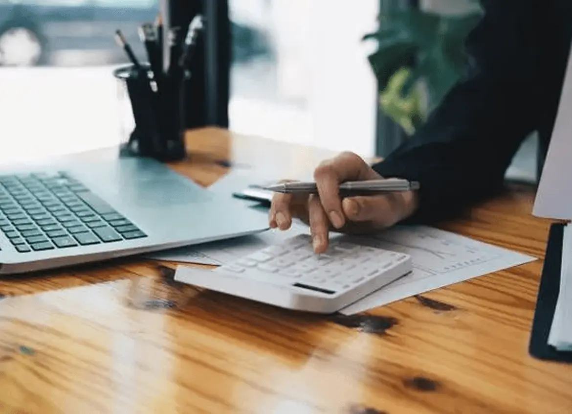 Person pointing at financial charts on paper by a laptop.