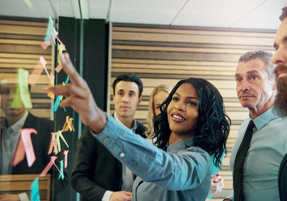 A woman points at a board while two colleagues watch attentively in a meeting.